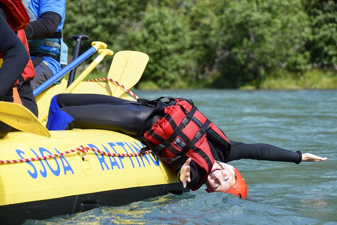 Young people leaning over the edge of the rafting boat so their heads go into the water